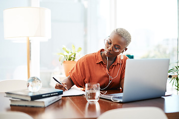 Image showing Dream big and do bigger. Shot of a young businesswoman wearing earphones while writing notes in an office.