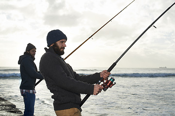 Image showing Secretly hoping hell hook the bigger fish...Shot of two young men fishing at the ocean in the early morning.