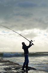 Image showing Taking his time for the big catch. Shot of a solo fisherman fishing off a pier at the ocean.