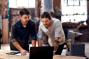 Image showing Teamwork divides the work and multiplies the success. Cropped shot of two handsome young using a laptop while working together inside their workshop.