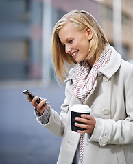 Image showing On the move and always in touch. Shot of an attractive woman standing outside holding a cup and reading a text message.