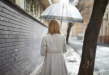 Image showing Not every day can be sunny. Rearview shot of a woman walking down a street in the rain and holding an umbrella.