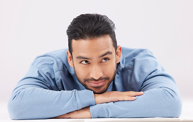 Image showing Thinking, dreaming and young man in a studio resting on his arms with a contemplating facial expression. Happy, smile and Indian male model with question or remember face isolated by white background