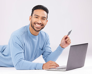 Image showing Laptop, credit card and asian man portrait on studio floor for ecommerce, sale or cashback on grey background. Online shopping, face and Japanese guy customer smile for loan, payment or sign up promo