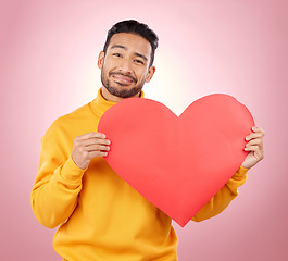 Image showing Heart, happy and love with portrait of man in studio for romance, date and valentines day. Kindness, support and hope with person and sign on pink background for wellness, peace and creative mockup