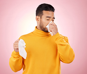 Image showing Sick, tissues and man blowing his nose in a studio with a cold, flu or sinus allergies. Illness, hayfever and Indian male person with paper napkin for virus or infection symptoms by a pink background