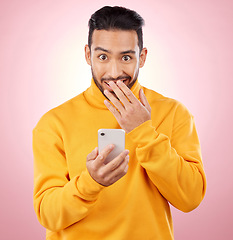 Image showing Phone, shock and portrait of a man in studio with a secret, gossip or fake news on social media. Male asian model with hand on mouth and smartphone for wow, surprise or chat on a pink background