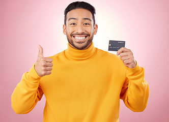 Image showing Man, thumbs up and credit card with finance, payment and loan, budget and fashion sale on studio pink background. Portrait, banking success and asian person or gen z for e commerce or shopping emoji