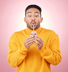 Image showing Food, cupcake and man blowing candle in studio for celebration, party and dessert. Birthday, wish and flame with face of male person and cake on pink background for surprise, candy and gift mockup