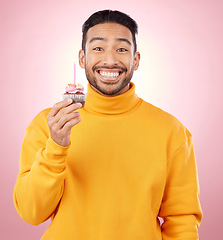 Image showing Man, portrait and cupcake for birthday, celebration and winner, success or achievement on pink background. Excited, happy and young asian person with candle and cake for winning competition in studio