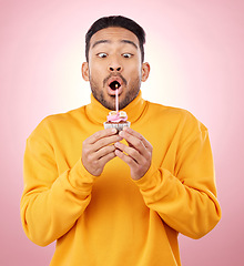 Image showing Birthday, cupcake and man blowing candle in studio for celebration, party and dessert. Food, wish and flame with face of male person and cake on pink background for surprise, candy and gift mockup