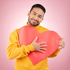 Image showing Heart, poster and love with portrait of man in studio for romance, date and valentines day. Kindness, support and hope with person and sign on pink background for wellness, peace and creative mockup