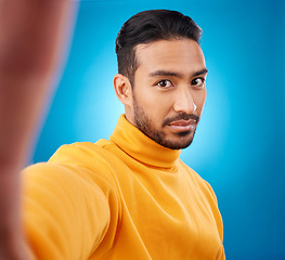 Image showing Selfie, face and portrait of a young man in studio with hand, style and fashion clothes. Serious male asian model on a blue background for social media, platform or network profile picture update