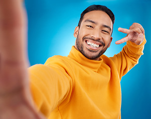 Image showing Selfie, happy and peace sign portrait of a man in studio with hand, emoji and a smile. Male asian fashion model on a blue background with a positive mindset for social media profile picture update