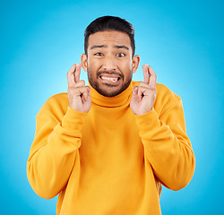 Image showing Nervous, portrait and fingers crossed by asian man with anxiety in studio for news, feedback or review on blue background. Hand, emoji and face of guy with stress for results, competition or giveaway