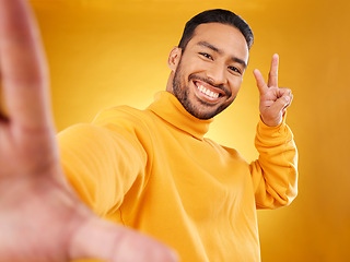 Image showing Selfie, peace sign and happy portrait of a man in studio with hand, emoji and a smile. Male asian fashion model on a yellow background with a positive mindset for social media profile picture update