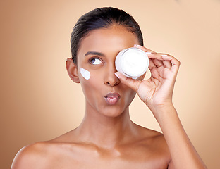 Image showing Woman, cream container thinking of eye skincare, dermatology health and cosmetics. Facial product, kiss face and young person or beauty model with skin care lotion on a studio, brown background