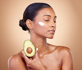 Image showing Woman, avocado and cream for skincare, natural beauty and vitamin c benefits on studio, brown background. Young calm person or model with facial, green fruits and skin care moisturizer in dermatology