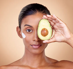 Image showing Woman, avocado and cream for face skincare, natural beauty or vitamin c benefits on studio, brown background. Young person or model in portrait for with green fruits, eye moisturizer and dermatology