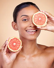 Image showing Skincare, woman and grapefruit on eye for beauty, cosmetics and natural product, health or vitamin c in portrait. Face of indian person or model, red fruit and dermatology on studio, brown background