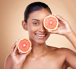 Image showing Beauty, woman and grapefruit on eye for skincare, cosmetics and natural product, health or vitamin c in portrait. Face of indian person or model, red fruit and dermatology on studio, brown background
