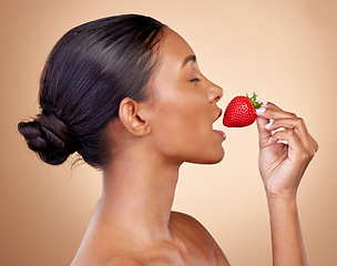 Image showing Beauty, strawberry and health of a woman in studio for wellness, cosmetics and dermatology. Fruit, diet and face of a young indian person on a brown background with natural makeup, glow and shine