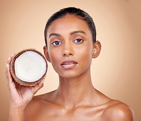 Image showing Woman face, coconut fruit and beauty, healthy skincare or vegan cream on brown studio background. Portrait of Indian person in natural product for dermatology, eco friendly cosmetics and oil benefits