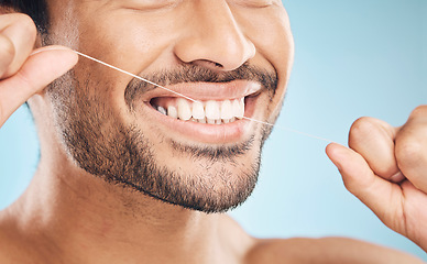 Image showing Wellness, teeth closeup and flossing of a man with cleaning and dental health in a studio. Face, blue background and healthy male person with dental floss for mouth hygiene and healthcare with smile