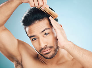 Image showing Portrait, beauty and a man brushing his hair on a blue background in studio for self grooming. Face, morning and routine with a young male model in the bathroom for style after shampoo treatment