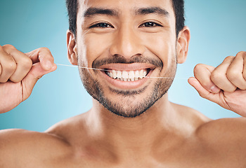 Image showing Wellness, teeth and flossing of a man portrait with cleaning and dental health in a studio. Face, blue background and healthy male person with dental floss for mouth hygiene and healthcare with smile