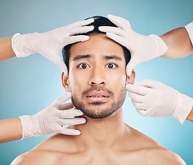 Image showing Portrait, hands and plastic surgery with a nervous man in studio on a blue background for beauty enhancement. Face, botox and change with a young male patient looking worried in a clinic for skincare