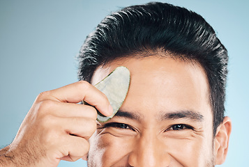 Image showing Closeup, man and beauty, gua sha and cosmetic tools, eyes and portrait with natural treatment on blue background. Skincare, glow and jade stone, dermatology and wellness with male model in studio