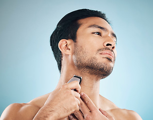 Image showing Face, shaving and electric razor with a man in studio on a blue background for personal hygiene, skincare or grooming. Beauty, wellness or cosmetics with a young male in the bathroom for hair removal