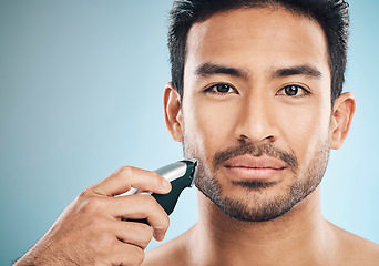 Image showing Portrait, shave and electric razor with a man in studio on a blue background for personal hygiene or grooming. Face, wellness or cosmetics with a confident young male in the bathroom for hair removal