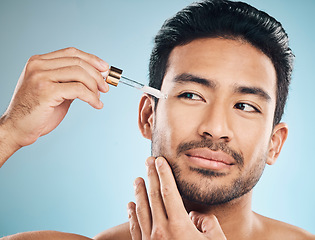 Image showing Face, beauty and antiaging oil with a man in studio on a blue background for skincare or grooming. Luxury, serum or wellness with a handsome male person in the bathroom to apply a product to his face