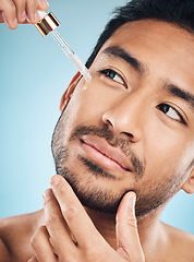 Image showing Face, skincare and antiaging serum with a man in studio on a blue background for beauty or grooming. Luxury, oil or wellness with a handsome young person in a bathroom to apply a product to his face