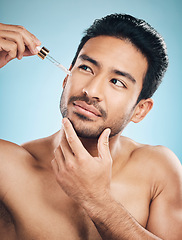 Image showing Face, beauty and antiaging serum with a man in studio on a blue background for skincare or grooming. Luxury, oil or wellness with a handsome male person in the bathroom to apply a product to his skin