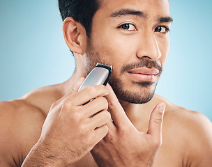 Image showing Portrait,, electric shaving and grooming with a man in studio on a blue background for personal hygiene or skincare. Face, wellness and cosmetics with a young male in the bathroom for hair removal