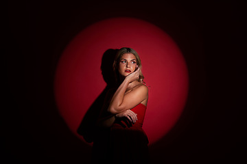 Image showing Fashion, spotlight and red with a model woman in studio on a dark background for classy elegance or style. Beauty, aesthetic and luxury with a confident young female person standing in a dress