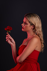 Image showing Beauty, fashion and woman with a rose on a dark, black background in a studio thinking of love, romance or red aesthetic. Girl with a flower, dress and formal style in fantasy, fairytale or art