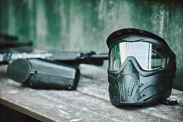 Image showing Paintball, helmet and gun on table at battle station of sports gear waiting for player, competition or war. Paint balling sportswear or stationary equipment ready for serious game, fight or warfare