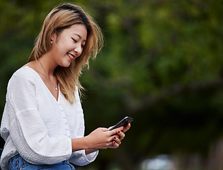 Image showing Happy woman, mockup and typing with phone in garden, reading email, social media meme or text. Cellphone, internet search and Asian girl in park space checking mobile app with smile and chat online.