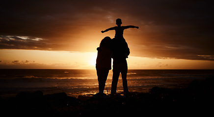 Image showing Sunset, beach and silhouette of parents with child by ocean for bonding, quality time and peace. Happy family, nature and back of mother, father and kid on shoulder on vacation, holiday and weekend