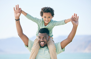 Image showing Black family, father and a son sitting on shoulders while outdoor in nature together during a beach vacation. Love, sky or kids with a parent carrying his male child while walking on the coast