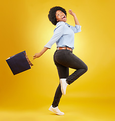 Image showing Bag, happy and black woman shopping, excited and celebrating sale in studio on yellow background. Discount, shopper and girl customer cheerful after boutique, retail or store deal posing isolated