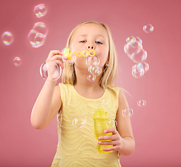 Image showing Portrait, fun and girl blowing bubbles, content and playing in studio while posing against pink background. Hand, face and child enjoying freedom, toy and innocent magic while standing isolated