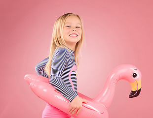 Image showing Happy, portrait and pool float with girl in studio for swimming, summer break or cute. Youth, funny and inflatable with child and flamingo ring for relax, smile or beach holiday on pink background