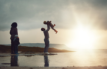 Image showing Sunset, view and a playing family on the beach together on a beautiful summer evening outdoor. Earth, water or nature with a mother, father and children bonding by the ocean or sea at the coast
