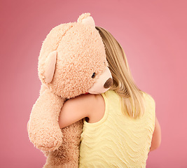 Image showing Teddy bear, love and back of a girl in a studio with a big, fluffy and cute toy as a gift or present. Adorable, innocent and young child hugging her teddy with care and happiness by a pink background