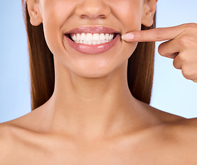 Image showing Dental, pointing and teeth with smile of woman in studio for beauty, clean and self care. Oral hygiene, natural and cosmetic treatment with girl model on blue background for veneers, fresh or results